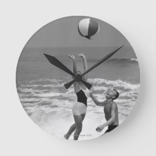 Paare, die mit einem Beachball spielen Runde Wanduhr