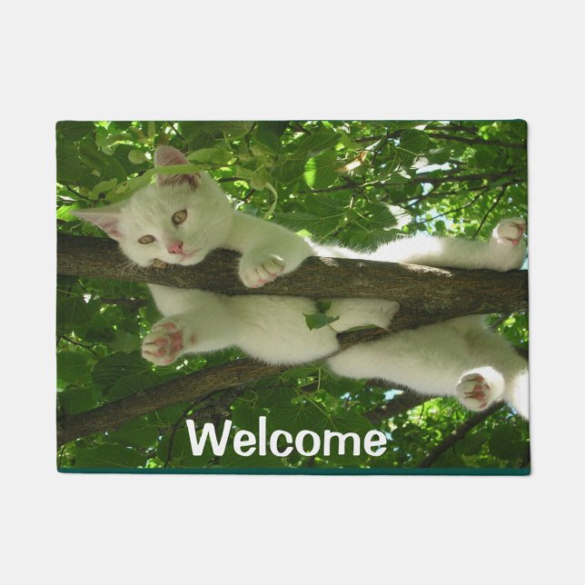 Paillasson Chat d'accueil ( A white kitten lying on a tree branch amidst lush green foliage.)