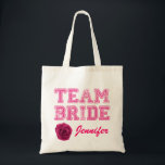 Pink Team Bride Tote Bag Tragetasche<br><div class="desc">Spaß Hochzeitsfeier Leinwand Tasche mit rosa Grafik Not Text lesen Team Bride. Benutzerdefinierter rosa Skripttext am unteren Rand ist bereit, für das gesamte Brautparty zu personalisieren. Die digitale Grafik einer rosa Rosenblüte schmückt den Boden links. Ideal, um alle wichtigen Dinge zu halten, die die Mitglieder des Brautparty nicht vergessen können....</div>