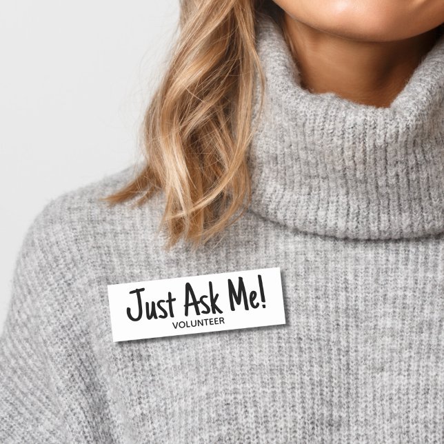 Porte-nom Volontaire Me Demandez Simple (Woman wearing gray sweater with black and white "just ask me" volunteer name tag badge.)