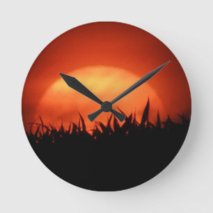 Roter Sonnenuntergang hinter schwarzem Gras Runde Wanduhr