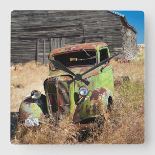 Rusting car in front of abandoned farm quadratische wanduhr