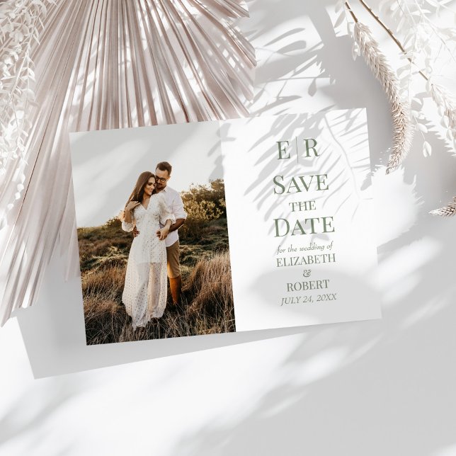 Save the Date Foto-Karte für Minimalistisches Oliv Einladung (Minimalist Olive Monogram Photo Save the Date Card on a sunny white table with dry botanicals.)