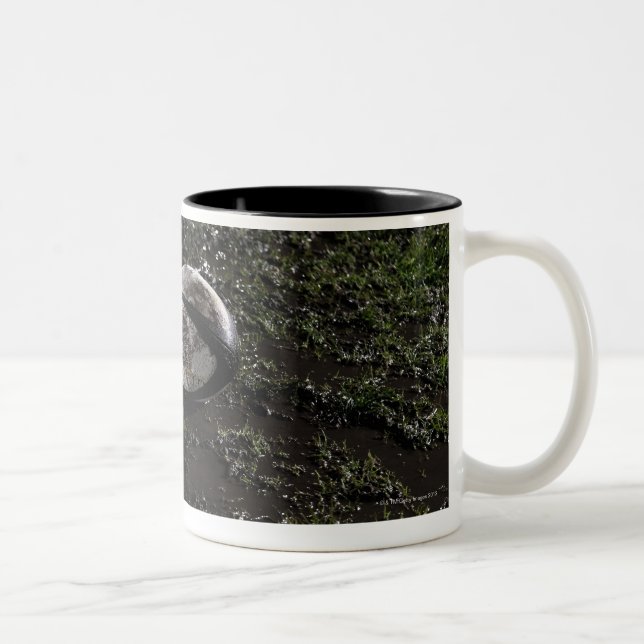 Schlammiger Rugbyball, der auf gekaut herauf Gras Zweifarbige Tasse (Rechts)