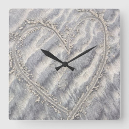 Schrulliges Herz, das im Sandquadrat zeichnet Quadratische Wanduhr
