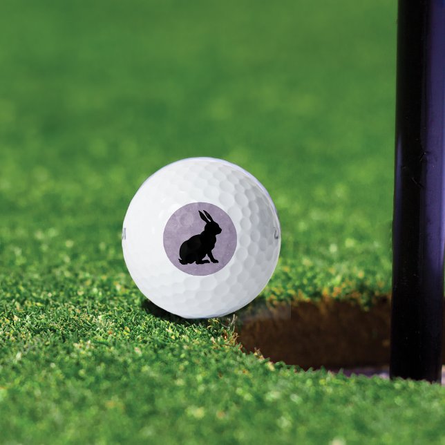 Schwarzes Kaninchen Silhouette Ostersonne Golfball (Black sitting rabbit in silhouette form on marbled light purple background on golf balls.)