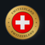 Schweizer Flagge Button<br><div class="desc">Die Schweizer Fahne ist in einen gerundeten Goldring der Imitate eingeprägt. Das Wort "Schweiz" steht ganz oben und unten im Design und hat einen gepressten Effekt. Das Paar von drei dekorativen Sternen zueinander,  sind auch mit einem gepressten Effekt gestaltet.</div>