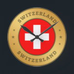 Schweizer Flagge Runde Wanduhr<br><div class="desc">Die Schweizer Fahne ist in einen gerundeten Goldring der Imitate eingeprägt. Das Wort "Schweiz" steht ganz oben und unten im Design und hat einen gepressten Effekt. Das Paar von drei dekorativen Sternen zueinander,  sind auch mit einem gepressten Effekt gestaltet.</div>