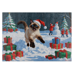 Siamkatze läuft im Schnee mit Weihnachtsmütze Schneidebrett