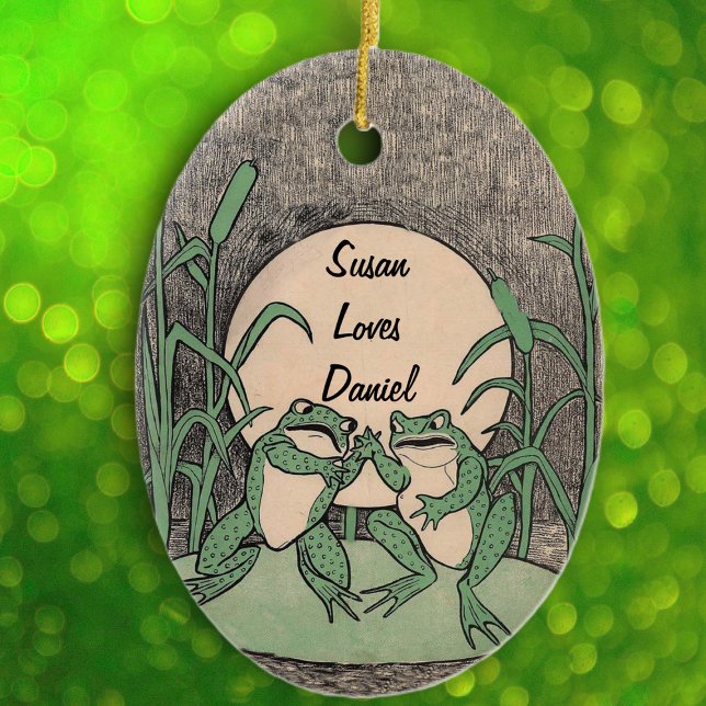 Spaß beim Streiten des grünen Froschpaares auf dem Keramikornament (Cute green fighting frogs on lily pad full moon reed plants on black white oval hanging ornament.)
