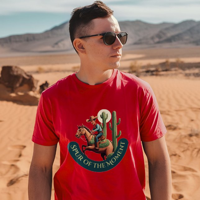 Spur des Augenblicks Cowboy Grafik T-Shirt (A man wearing a cardinal t-shirt with a cowboy and cactus design stands in a desert landscape)