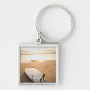 Surfbrett, das auf Strand am Sonnenuntergang legt Schlüsselanhänger