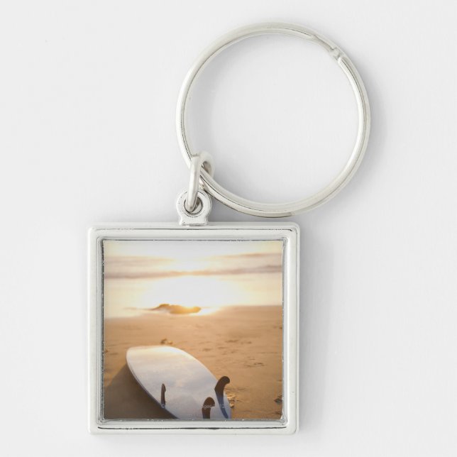 Surfbrett, das auf Strand am Sonnenuntergang legt Schlüsselanhänger (Vorne)