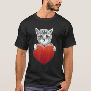Süßes Katzenbaby hält großes rotes Herz zwischen d T-Shirt