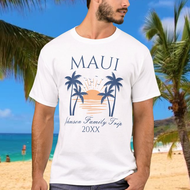 T-shirt Voyage Famille Maui (Man wearing a Maui family trip t-shirt with a sunset and palm tree design, standing on a beach.)