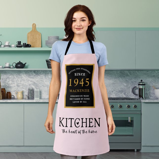 Tablier 80e Anniversaire Cuisine Queen Coeur de maison ros (Personalized 80th birthday pink apron worn by a woman in the kitchen)