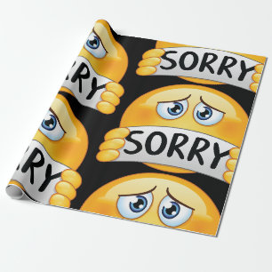 Trauriges Sorry Emoji Gesicht hält Entschuldigungs Geschenkpapier