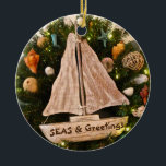 Tropical Coastal SEAS & Greetings Beach Christmas Keramik Ornament<br><div class="desc">Christmas by the Sea! Add this stunning coastal-inspired Ceramic Ornament to your tropical-themed holidays. The photo image on the Ornament features a wreath adorned with starfish, various types of seashells, rattan balls, fruit, and a sailboat. The color palette is soothing earth tones of brown and tan. The text reads: "SEAS...</div>