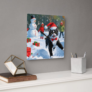 Tuxedo-Katze läuft im Schnee mit Weihnachtshut Quadratische Wanduhr