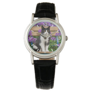 Tuxedo Katze sitzt auf einem Gartenstuhl mit Blume Armbanduhr