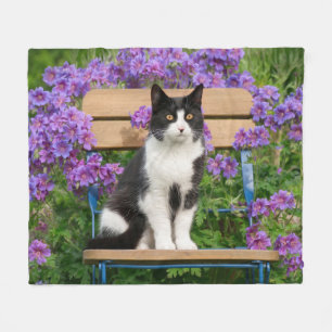 Tuxedo Katze sitzt auf einem Gartenstuhl mit Blume Fleecedecke