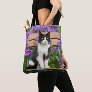 Tuxedo Katze sitzt auf einem Gartenstuhl mit Blume Tasche
