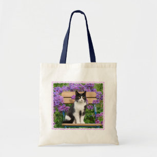 Tuxedo Katze sitzt auf einem Gartenstuhl mit Blume Tragetasche