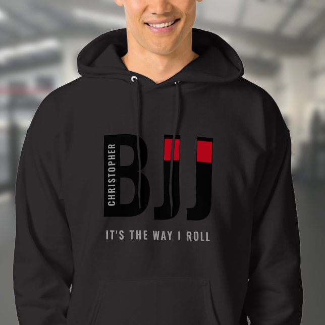 Veste À Capuche BJJ Brazil Jiu Jitsu Ajouter Nom Ceinture noire (Unisex black BJJ hoodie worn by male model in a gym.)