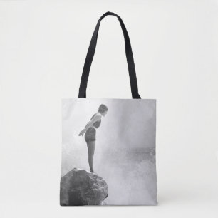 Weibliche Schwimmerin auf Felsen über tosenden Wel Tasche