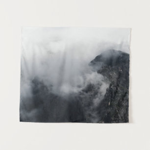 Weiße Wolken über den dunklen felsigen Bergen Wandteppich