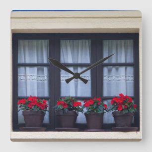 Wohnhaus mit Blumen in den Fenstern Quadratische Wanduhr