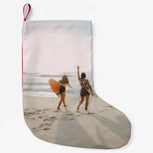 Zwei Frauen, die zum Ozean laufen und surfen Kleiner Weihnachtsstrumpf