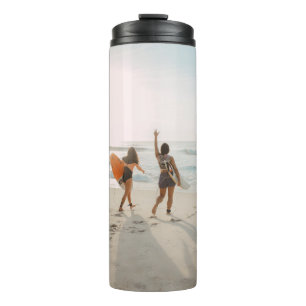 Zwei Frauen, die zum Ozean laufen und surfen Thermosbecher